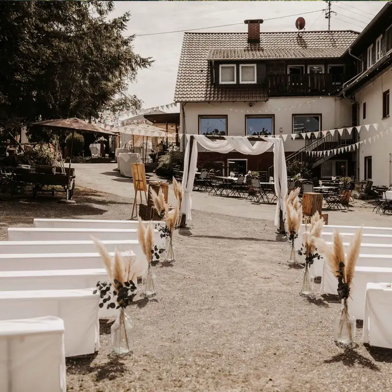 Trauung im Freien bei der Pension Mausmühle Romantisch dekorierte Outdoor-Hochzeitslocation vor der Pension Mausmühle mit Traubogen, Bänken und festlicher Atmosphäre.