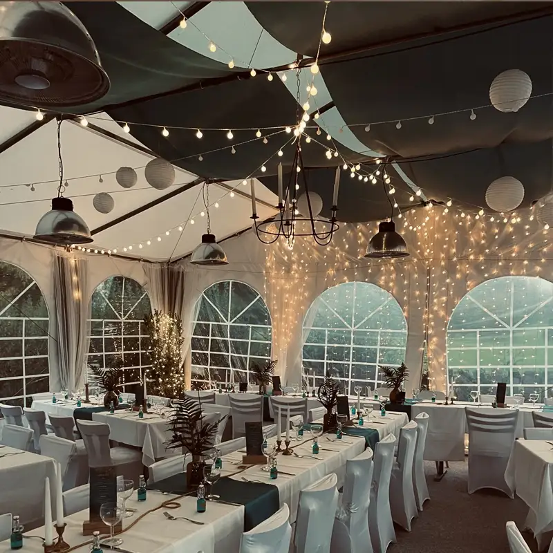 Romantische Hochzeitsfeier am Abend im festlich geschmückten Zelt Stimmungsvoll beleuchtetes Hochzeitszelt mit Lichterketten, festlich gedeckten Tischen und eleganter Dekoration für eine Abendfeier.