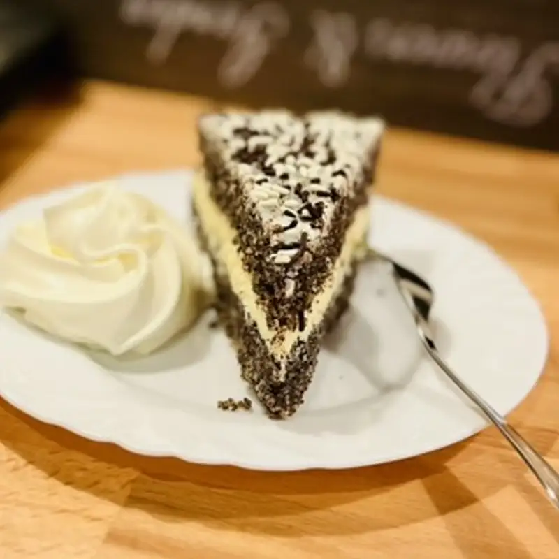 Hausgemachte Mohntorte mit Vanillecreme im Café Mausmühle Stück Mohntorte mit Vanillecreme und Sahne auf weißem Teller im Café Mausmühle.