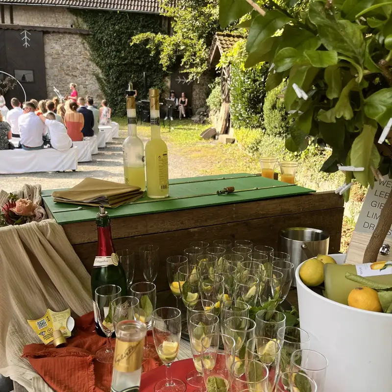 Erfrischende Getränkebar bei Feier in der Mausmühle im Westerwald Getränkebar mit Zitronenlimonade und Sekt bei einer Feier in der Pension Mausmühle im Westerwald, im Hintergrund Gäste bei einer Zeremonie.