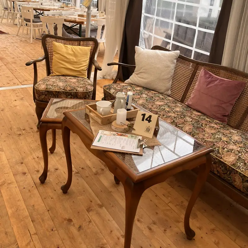 Charmante Vintage-Ecke im Hochzeitszelt der Mausmühle Gemütliche Vintage-Sitzgruppe mit floralen Polstern und Holztischen im dekorierten Hochzeitszelt der Mausmühle.