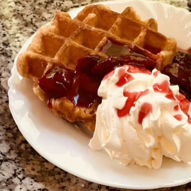Hausgemachte Waffel mit Kirschen und Sahne im Café Mausmühle Frisch gebackene Waffel mit heißen Kirschen und Sahne auf einem weißen Teller im Café Mausmühle.